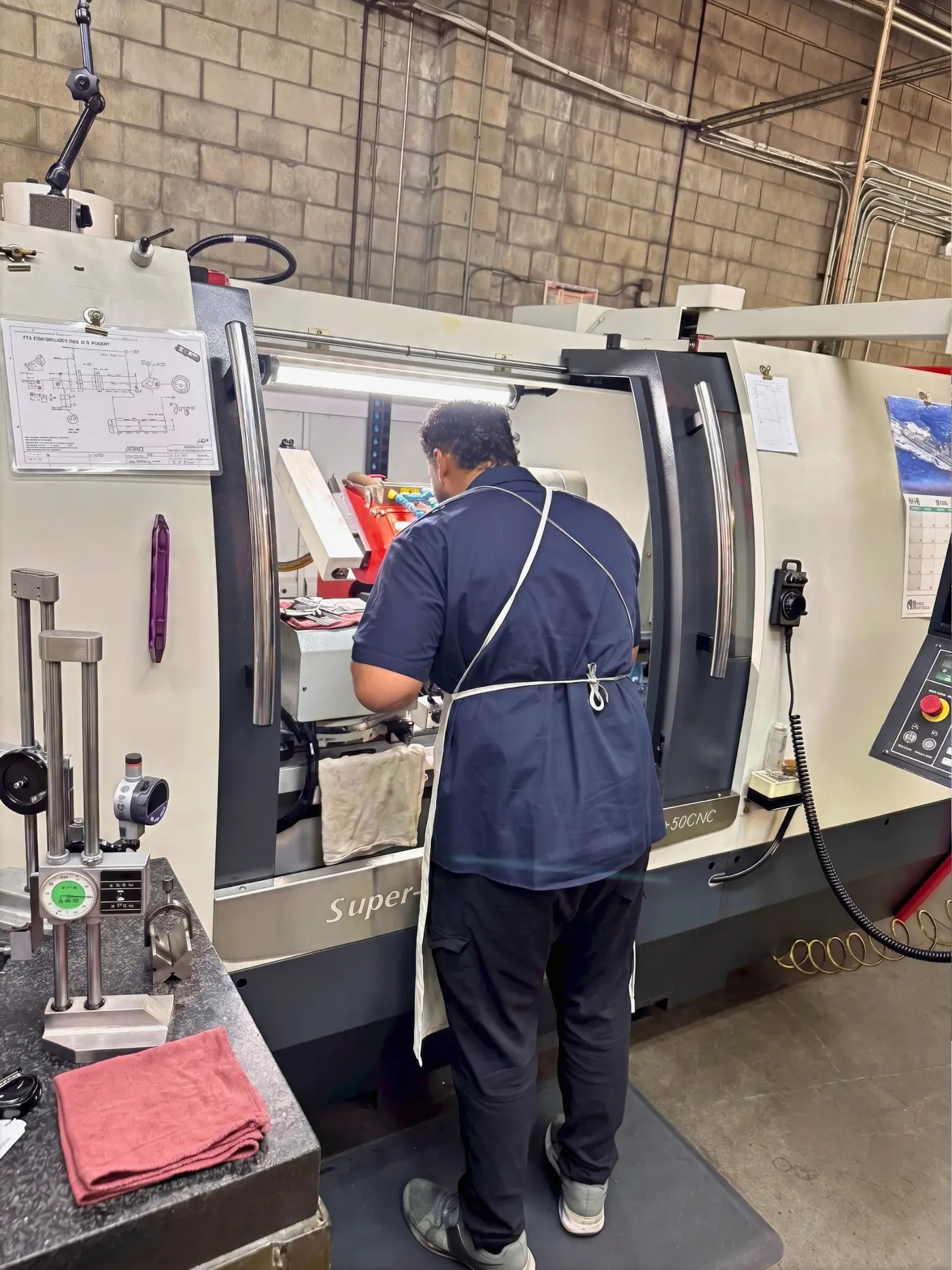 Tim Ramos working at the CNC cylindrical grinder, print clipped to the machine